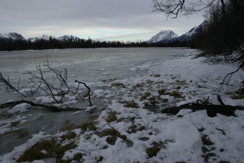 2003 Jeep TJ - A winter scene shows a partially frozen lake with snow and ice on the shore, backed by a treeline and snow-capped mountains.