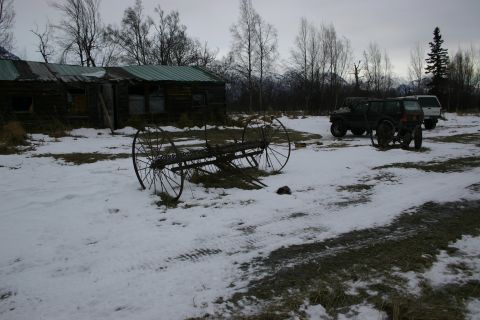 2003 Jeep TJ - Two SUVs and vintage farm equipment sit in the snow near a rustic cabin.