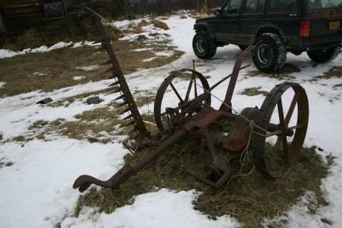 2003 Jeep TJ - A black Jeep Cherokee is parked behind a rusty, old farm implement in a snowy, outdoor setting.