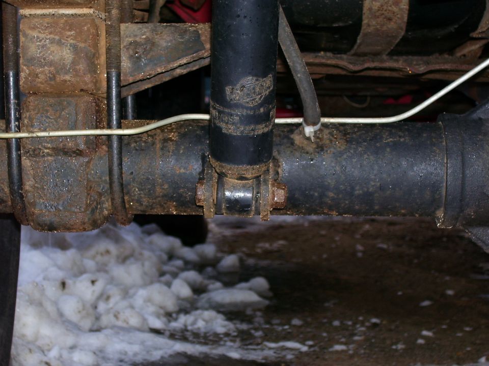 Underneath view of rear axle with shock absorber mount, U-bolts, and brake line over snowy ground