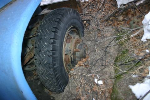 2003 Jeep TJ - A vehicle's wheel and suspension are visible in a natural outdoor setting with dirt, leaves, and snow.