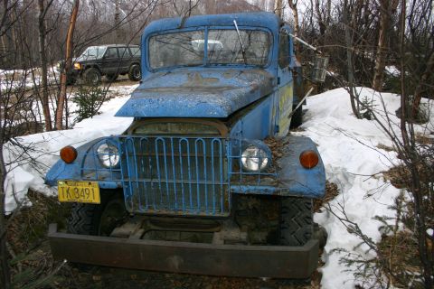 2003 Jeep TJ - An old blue truck sits in the snow, with a dark SUV in the background.