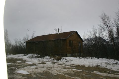 2003 Jeep TJ - A rustic wooden cabin sits in a winter landscape with snow on the ground and bare trees surrounding it.