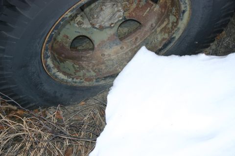 2003 Jeep TJ - A close-up view of a vehicle's wheel and tire, partially obscured by snow and dry vegetation.