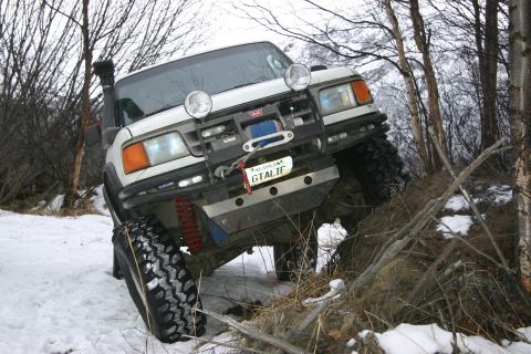 2003 Jeep TJ - An off-road SUV navigates a snowy, wooded trail with a snorkel and winch visible.