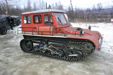 2003 Jeep TJ - A vintage red tracked vehicle sits in the snow, with a dark SUV nearby.