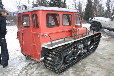 2003 Jeep TJ - A red tracked vehicle is parked next to a white Jeep in a snowy environment.