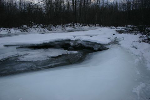 2003 Jeep TJ - A partially frozen river flows through a wooded area with snow on the banks.