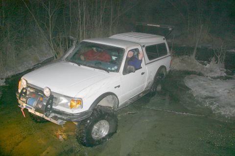 2003 Jeep TJ - A white pickup truck navigates through a watery and icy terrain at night.