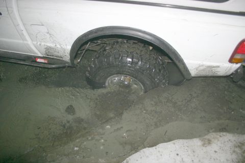 2003 Jeep TJ - A white pickup truck is stuck in mud, with its rear tire deep in the mire.