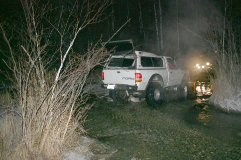 2003 Jeep TJ - White Ford pickup truck navigates shallow water at night, with another vehicle's lights visible ahead.
