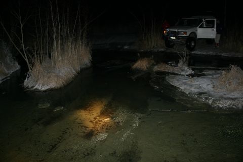 2003 Jeep TJ - A white pickup truck is parked on the side of a dark, icy stream at night.