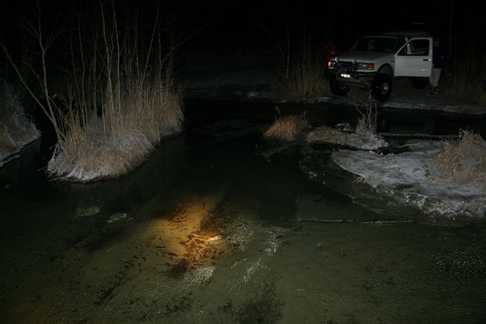 White pickup truck with open driver's door, parked on icy bank next to a dark stream