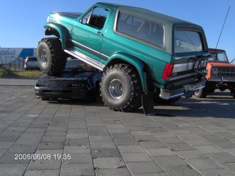 1996 Ford Bronco - A lifted green Ford Bronco is parked on top of a black car, with another Bronco visible behind it.