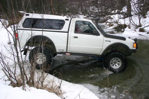 2003 Jeep TJ - A white Ford Ranger pickup truck navigates a winter stream with a snorkel and camper shell.