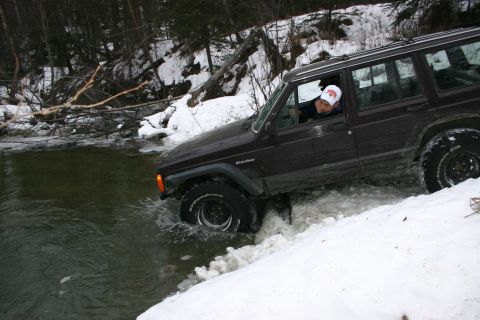 2003 Jeep TJ - A dark brown Jeep Cherokee XJ navigates a snowy and watery trail in a wooded area.
