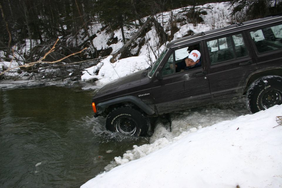 Dark brown Jeep Cherokee XJ driving through water and snow on a wooded trail
