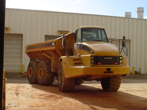 1966 International School Bus - A Caterpillar 740 articulated dump truck is shown from the front, parked on a dirt lot in front of a large building.