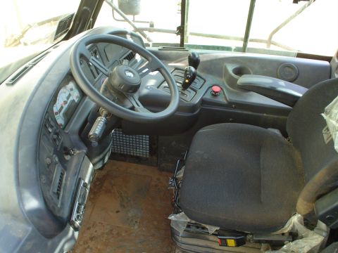 1966 International School Bus - The interior of a truck cab shows the steering wheel, dashboard gauges, and a seat with "CAT" branding visible.