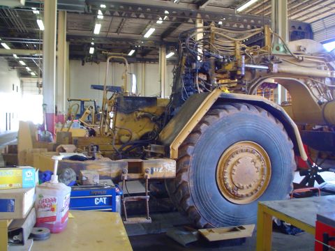 1966 International School Bus - A large yellow construction vehicle is seen in a repair shop, with its engine components exposed and a CAT toolbox nearby.