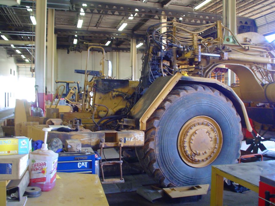 Yellow heavy equipment vehicle with large tire in repair shop. CAT toolbox visible