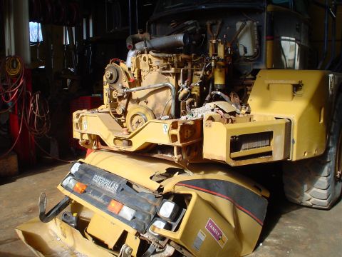 1966 International School Bus - A Caterpillar articulated dump truck's engine and front chassis are visible, with the front end showing significant damage.