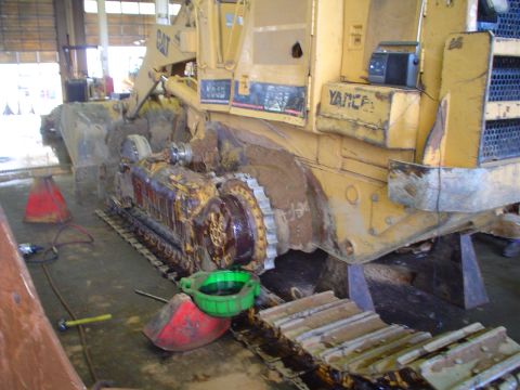 1966 International School Bus - A yellow bulldozer is parked indoors, undergoing maintenance with tools and oil pans scattered around.