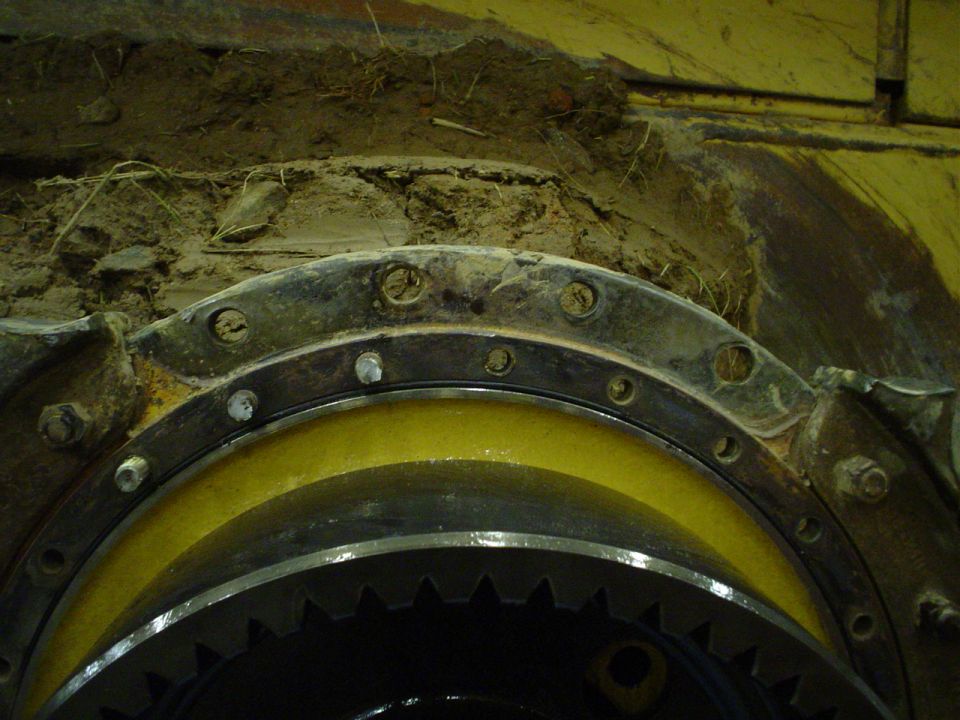 Close-up of heavy machinery gears and bolted flange, covered in dirt