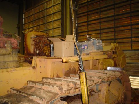 1966 International School Bus - A yellow bulldozer sits in a workshop, its engine compartment open and batteries visible on top.