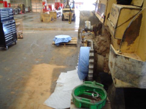 1966 International School Bus - A green oil drain pan sits on the floor next to the tracks of heavy machinery in a workshop.