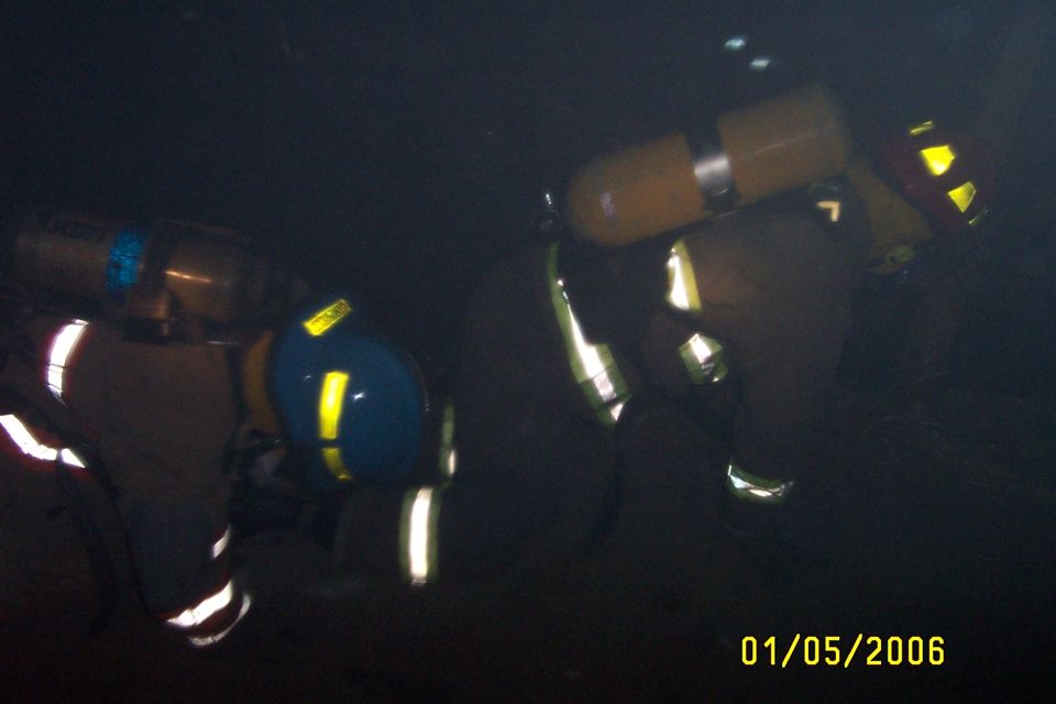 Firefighters in turnout gear with SCBA bottles crouched in a dark training space