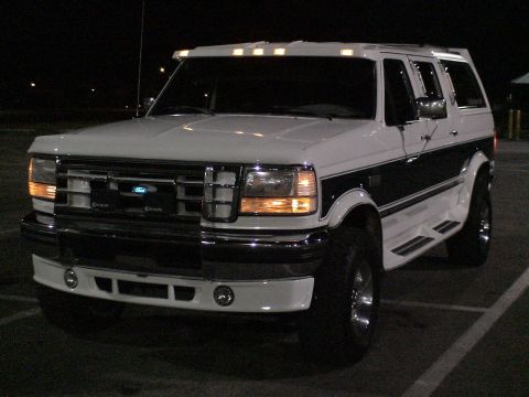 1993 Ford C-350 (Centurion Conversions) - White Ford truck with dark side stripe and Centurion conversion package, front 3/4 view at night.