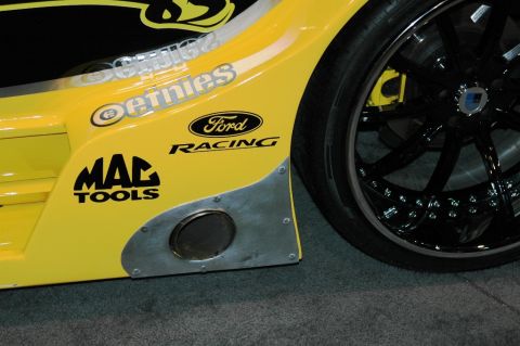 1991 Ford Taurus - Close-up of a yellow race car's side, racing decals and a prominent exhaust outlet.
