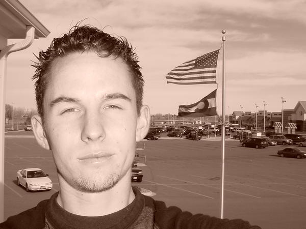 Man in foreground, American and Colorado flags, parking lot with cars