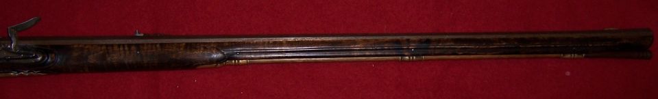 Flintlock rifle side view, dark wood stock with metal components, red background