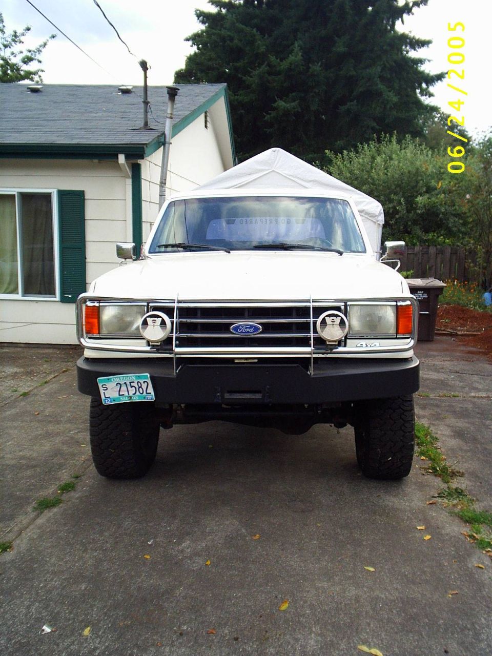 Front view of white lifted 1990 Ford Bronco with black bumper, brush guard, and Oregon plate 21582 in a driveway