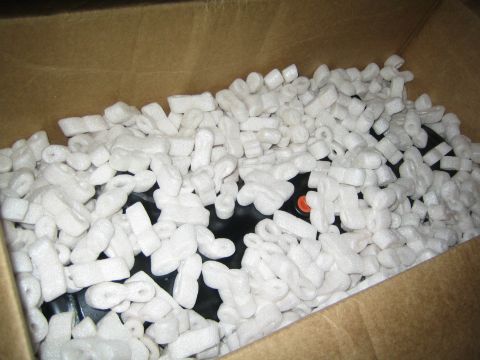 1990 Ford Bronco - black object, possibly a winch, lies buried in white foam packing peanuts inside an open cardboard shipping box.