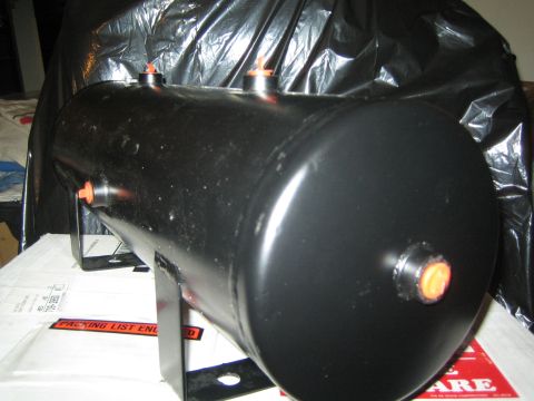 1990 Ford Bronco - black horizontal air reservoir tank with several threaded ports and mounting feet rests on a draped surface beside paperwork.