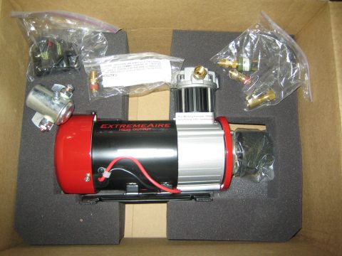 1990 Ford Bronco - red and chrome ExtremeAire high-output air compressor sits in foam packaging surrounded by bagged fittings and hardware.