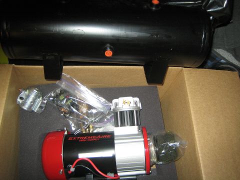 1990 Ford Bronco - ExtremeAire compressor in foam packaging with bagged fittings, a black air tank positioned just above in a cardboard box.