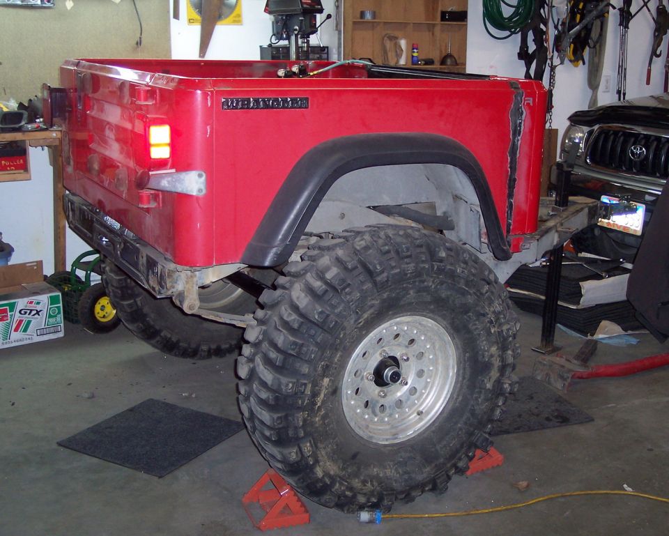 Stripped red Jeep Wrangler tub on oversized mud tires in a garage, rear three-quarter view