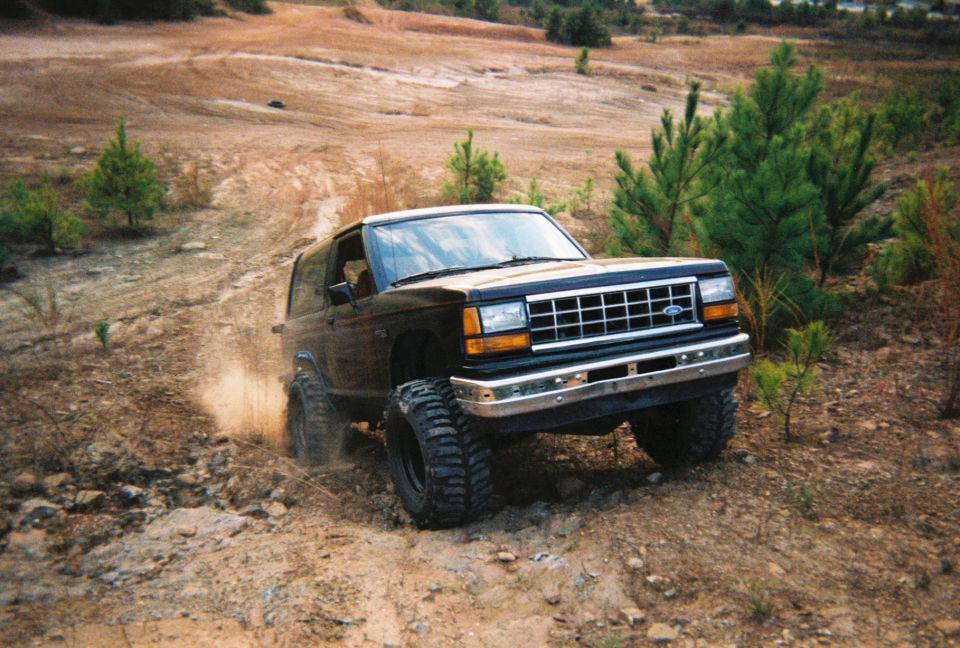Lifted black Ford Bronco II on big off-road tires climbing a rocky dirt trail
