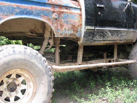 1992 Ford Bronco - The undercarriage of a heavily modified off-road vehicle shows extensive rust and mud accumulation.