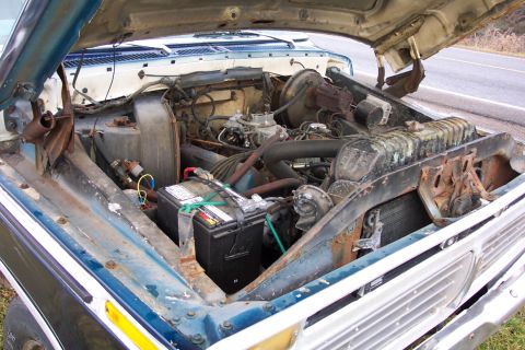 1975 Ford F-150 - The engine bay of a 1975 Ford F-150 is visible with the hood raised, showing the engine and battery.