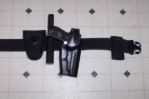 1998 Ford Crown Victoria - A black duty belt is equipped with a holstered handgun and a baton, laid out on a tiled surface.