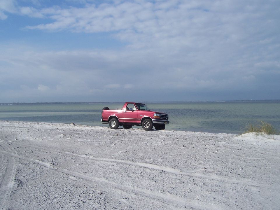 Red SUV parked on a sandy beach next to the ocean