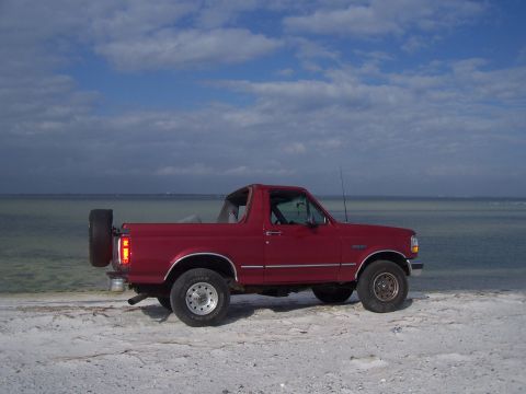 1995 Ford Bronco - A red Ford Bronco is parked on a beach with the ocean in the background.