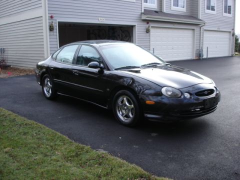 1998 Ford Taurus - Black Ford Taurus sedan on alloy wheels parked in a driveway in front of a townhouse garage.