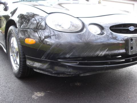 1998 Ford Taurus - The front of a black 1998 Ford Taurus shows extensive damage to the bumper.