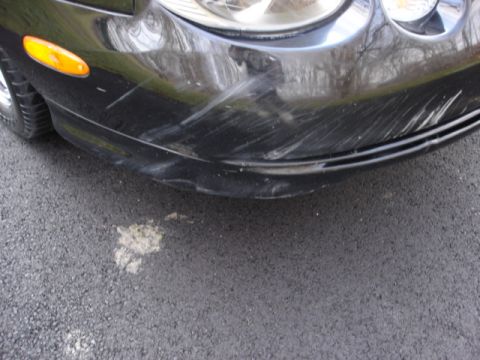 1998 Ford Taurus - Front bumper of a black car with significant scratches and damage to the lower edge.